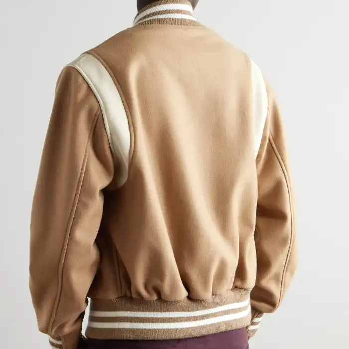 A person's back wearing a beige and camel wool varsity jacket with leather detailing and striped collar.