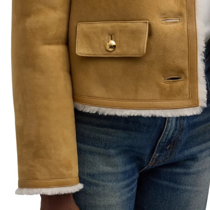 Close-up of a brown suede jacket with a gold button and white trim, worn over blue jeans.